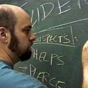 Balding, bearded man writing on a chalkboard